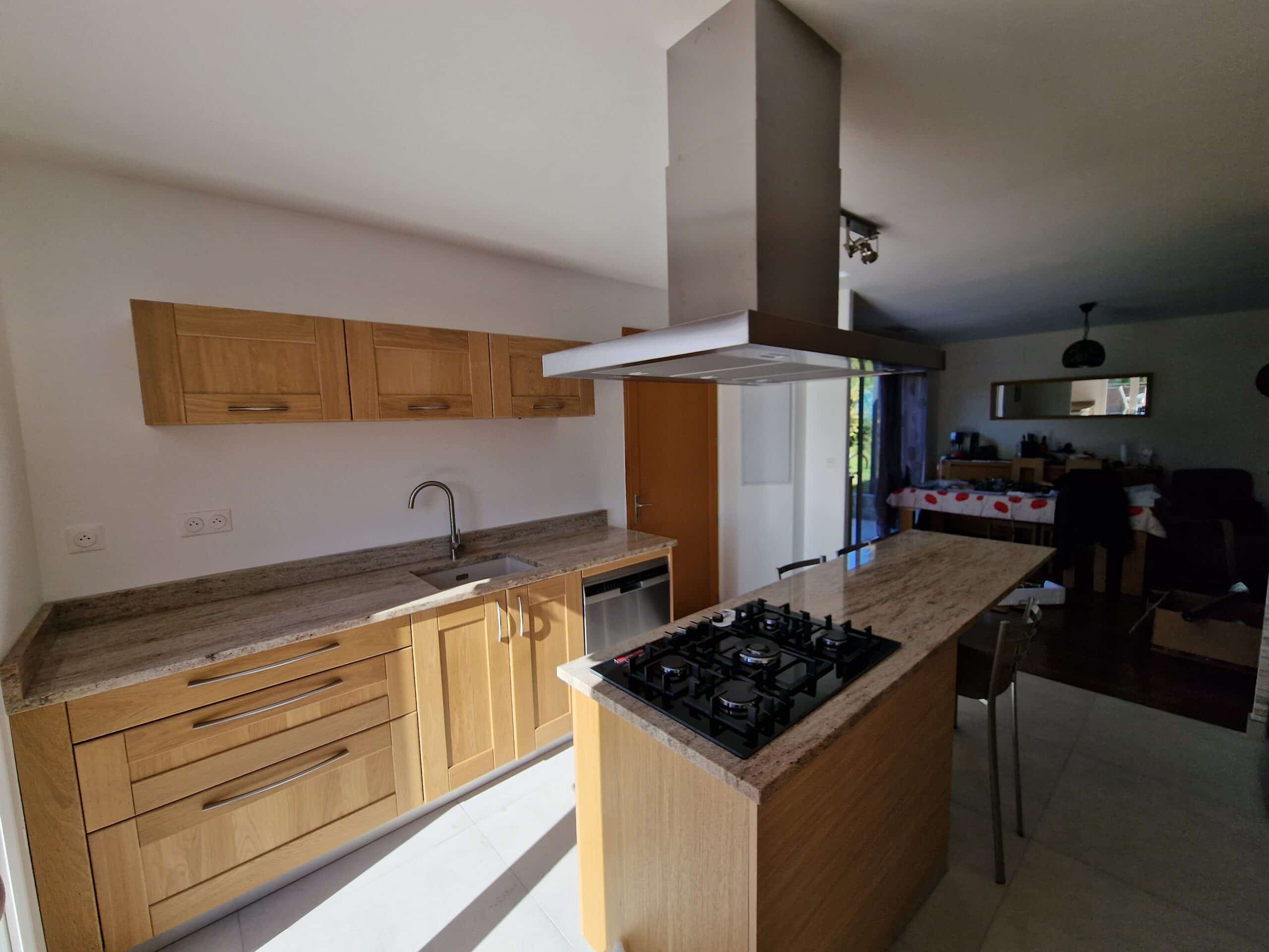 Cuisine moderne en bois avec îlot central en granite, plaques de cuisson au gaz et hotte aspirante en inox.