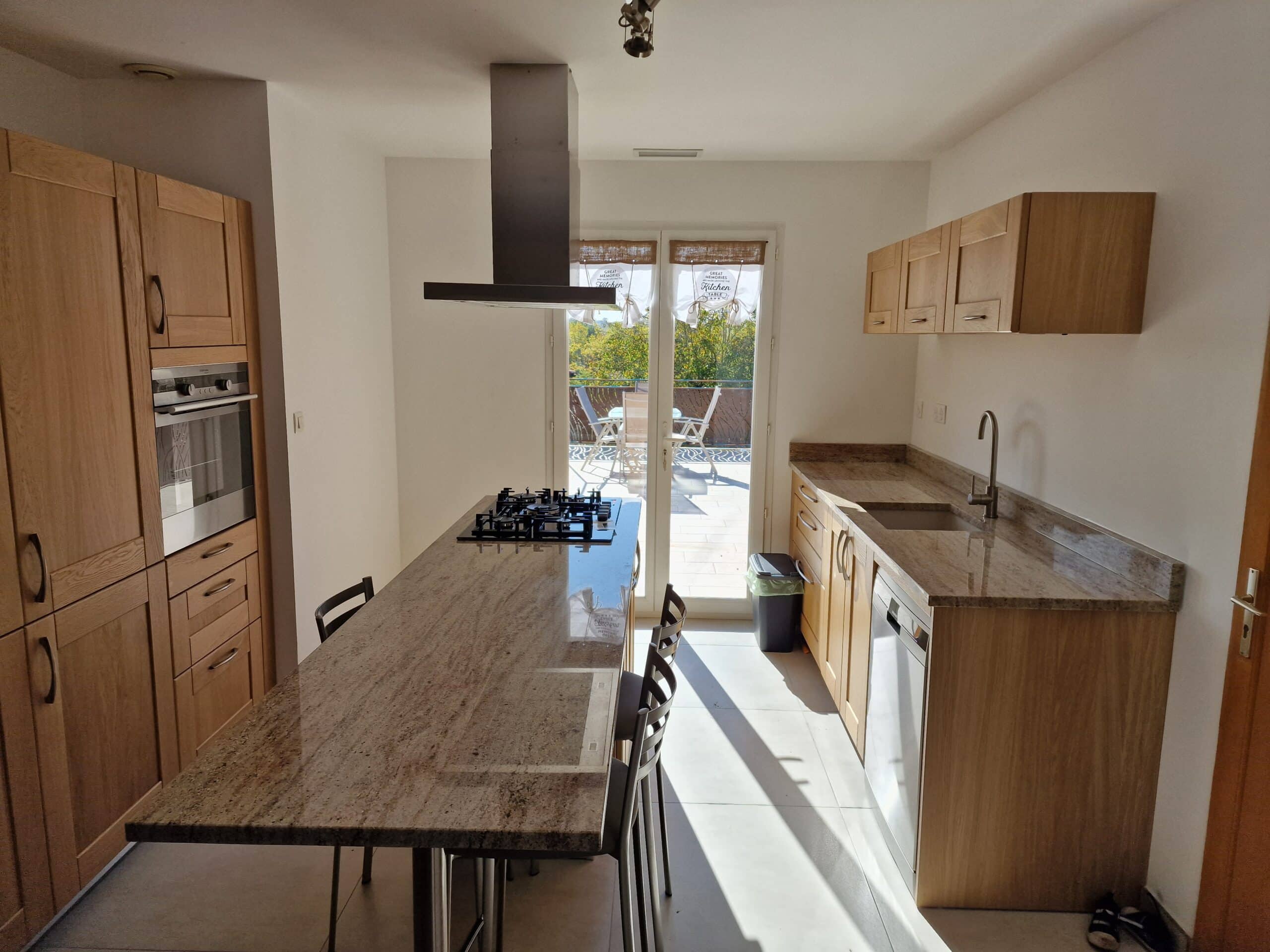 Cuisine moderne lumineuse, îlot en granit, meubles bois, accès balcon. Rideaux Great Memories Kitchen Table.