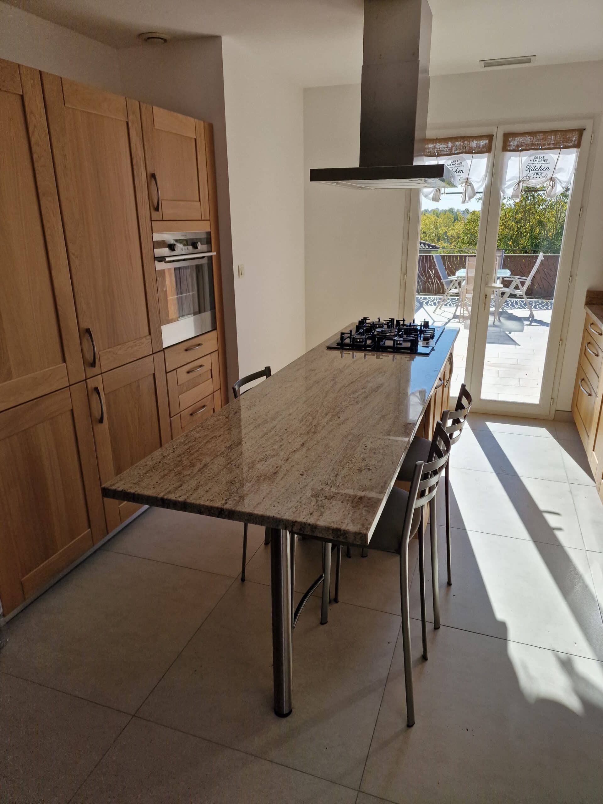 Cuisine moderne avec îlot en granit, meubles en chêne et message 'Great memories are made around the kitchen table'.