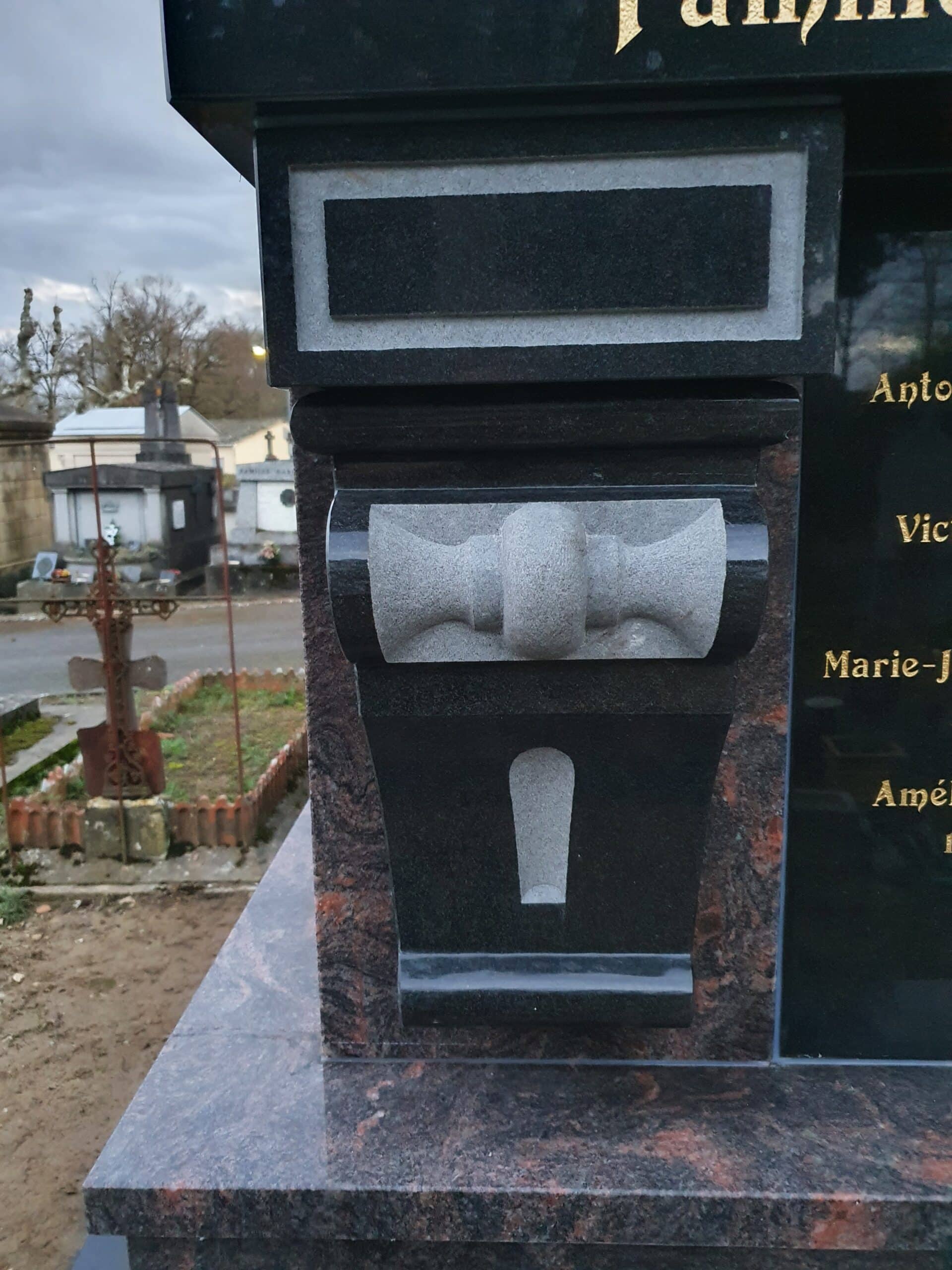 Sculpture décorative grise sur stèle funéraire en granit noir poli, noms gravés en or sur le côté dans un cimetière.