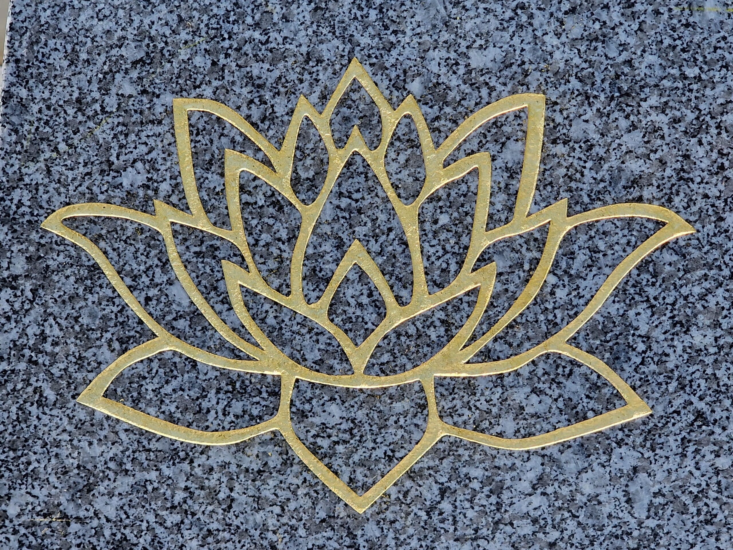Fleur de lotus dorée stylisée aux contours épurés sur un fond de granit gris moucheté élégant.