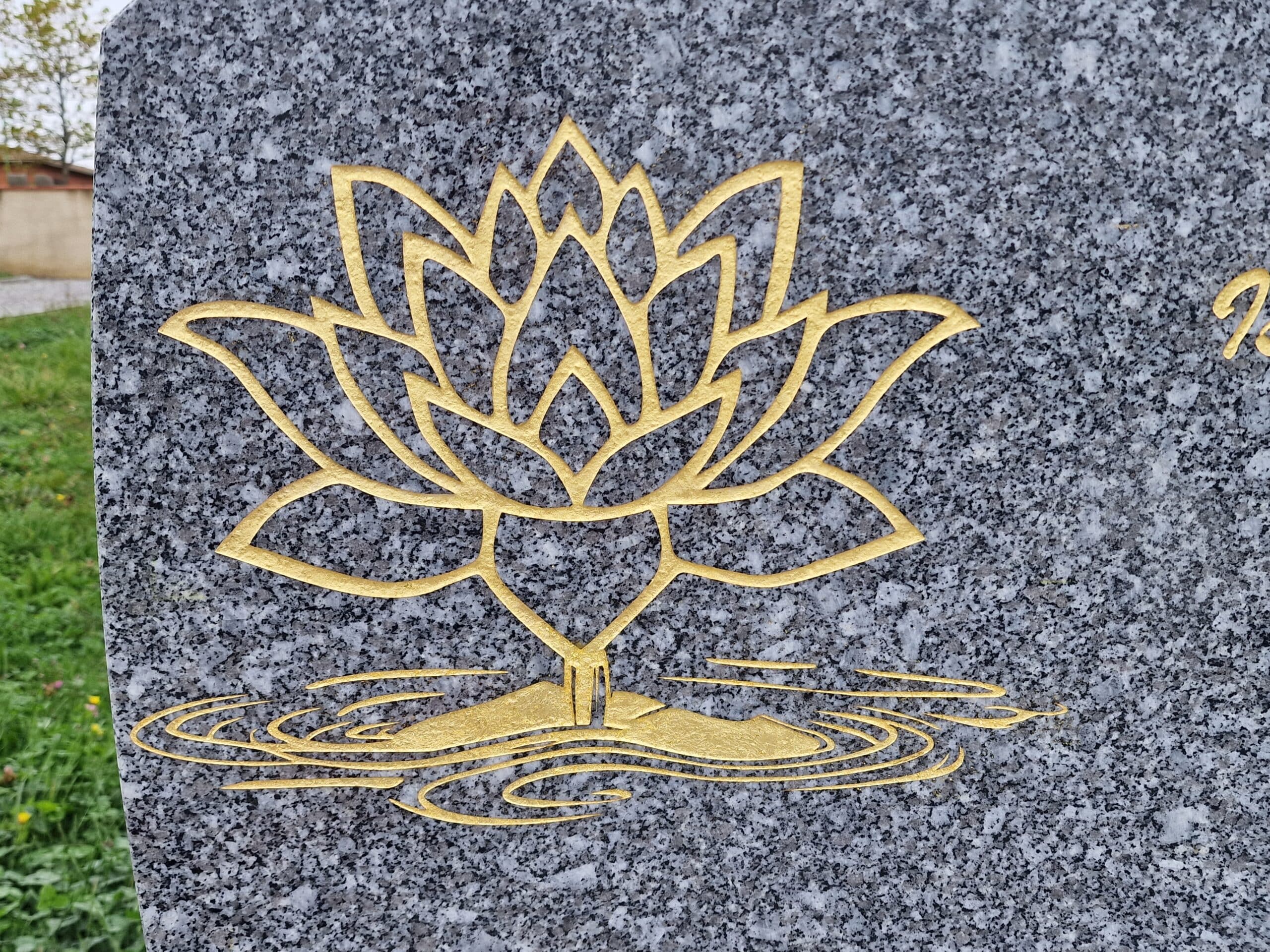 Fleur de lotus stylisée dorée gravée sur un monument en granit gris avec des ondulations d'eau à sa base.
