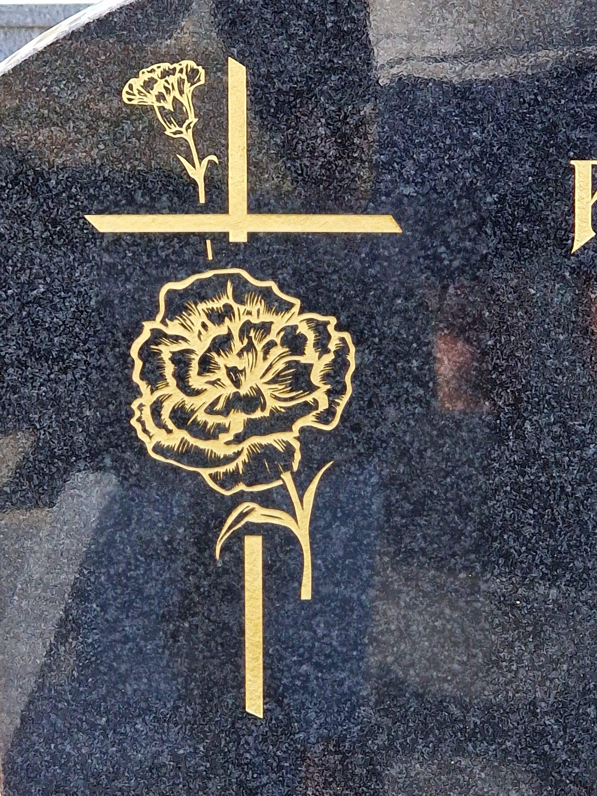 Croix et œillets dorés gravés sur granit noir poli, symboles de deuil et de mémoire éternelle.