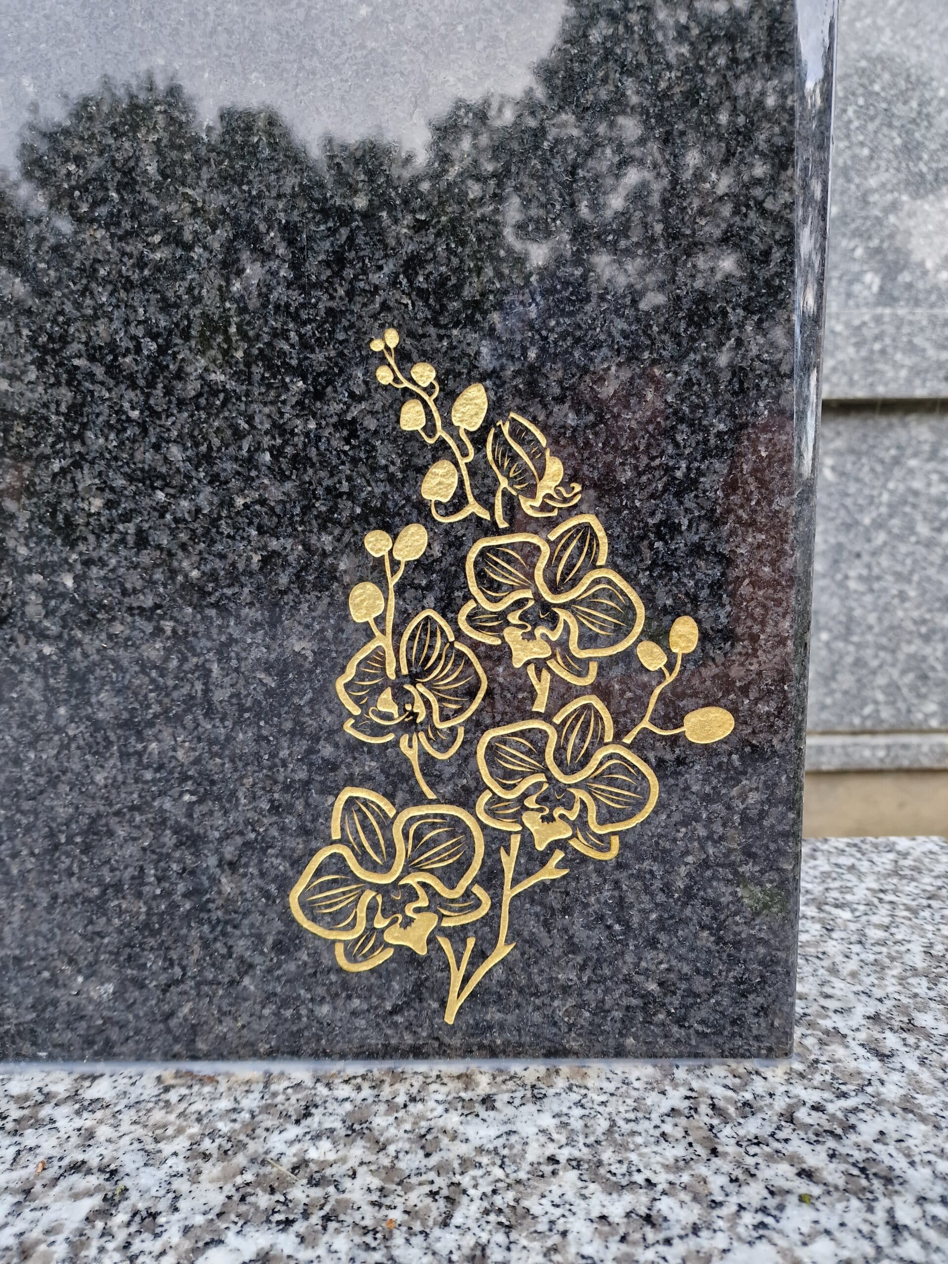 Orchidées gravées à la feuille d'or sur une stèle en granit noir poli.