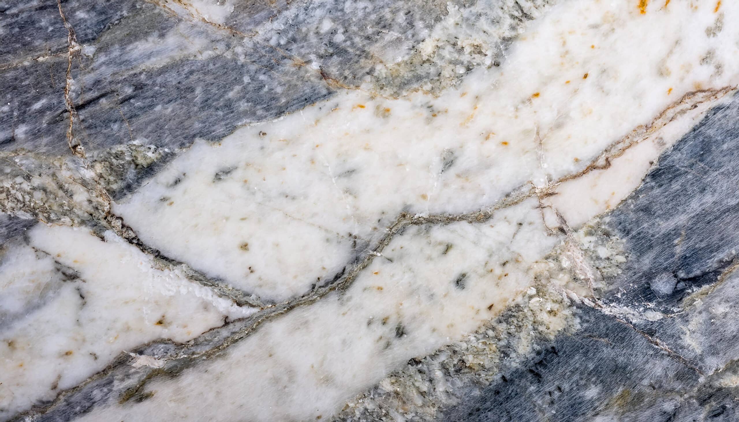 Texture de marbre veiné aux tons gris, blanc et ocre, traversée par des fissures naturelles complexes.