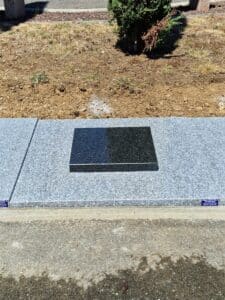 Plaque funéraire en granit noir poli sur socle gris par la Marbrerie Régis Seguela, installation dans un cimetière.