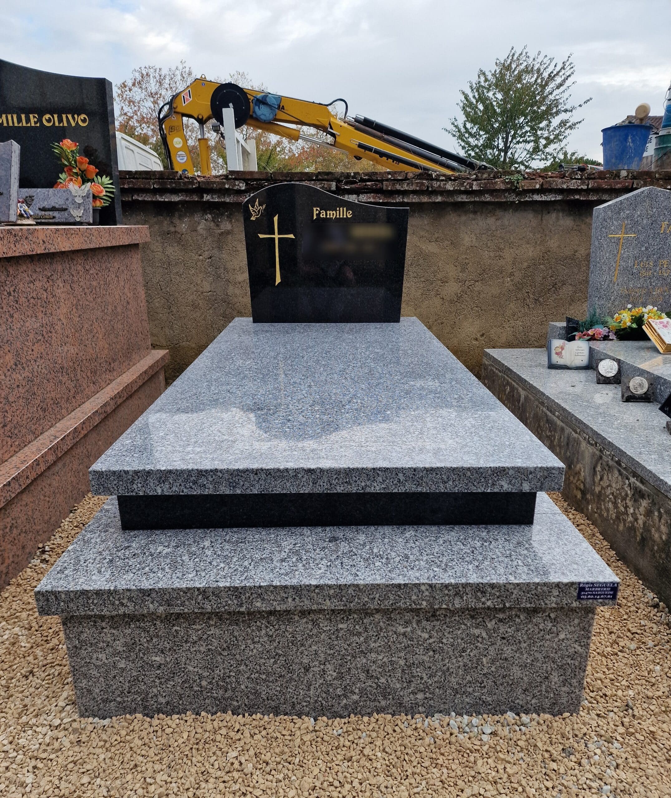 Monument funéraire en granit bicolore noir et gris avec une croix dorée et l'inscription Famille dans un cimetière.