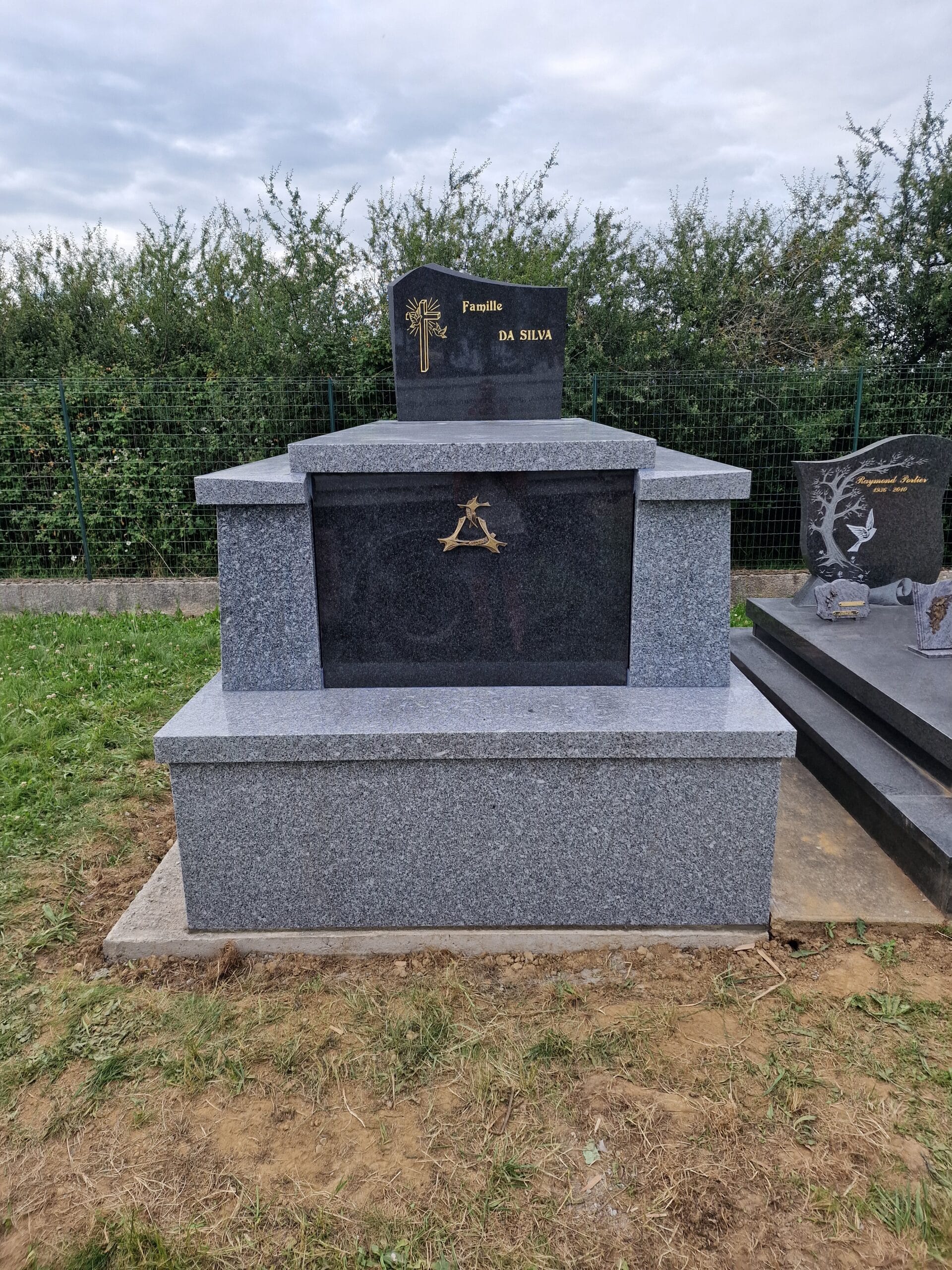 Monument funéraire en granit gris et noir de la Famille Da Silva avec croix dorée et emblème dans un cimetière.