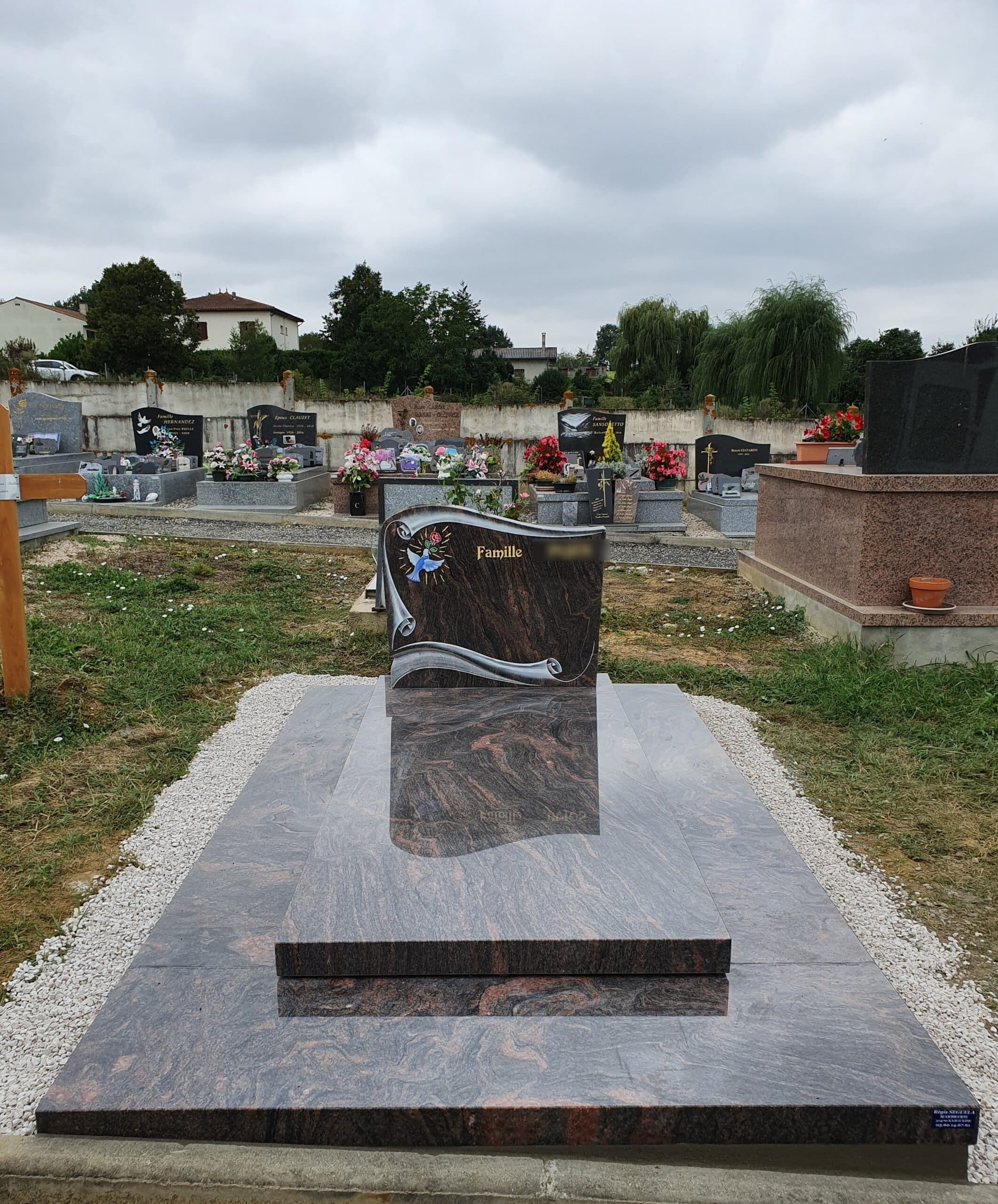 Monument funéraire en granit poli marbré avec inscription Famille et oiseau bleu dans un cimetière paysager.