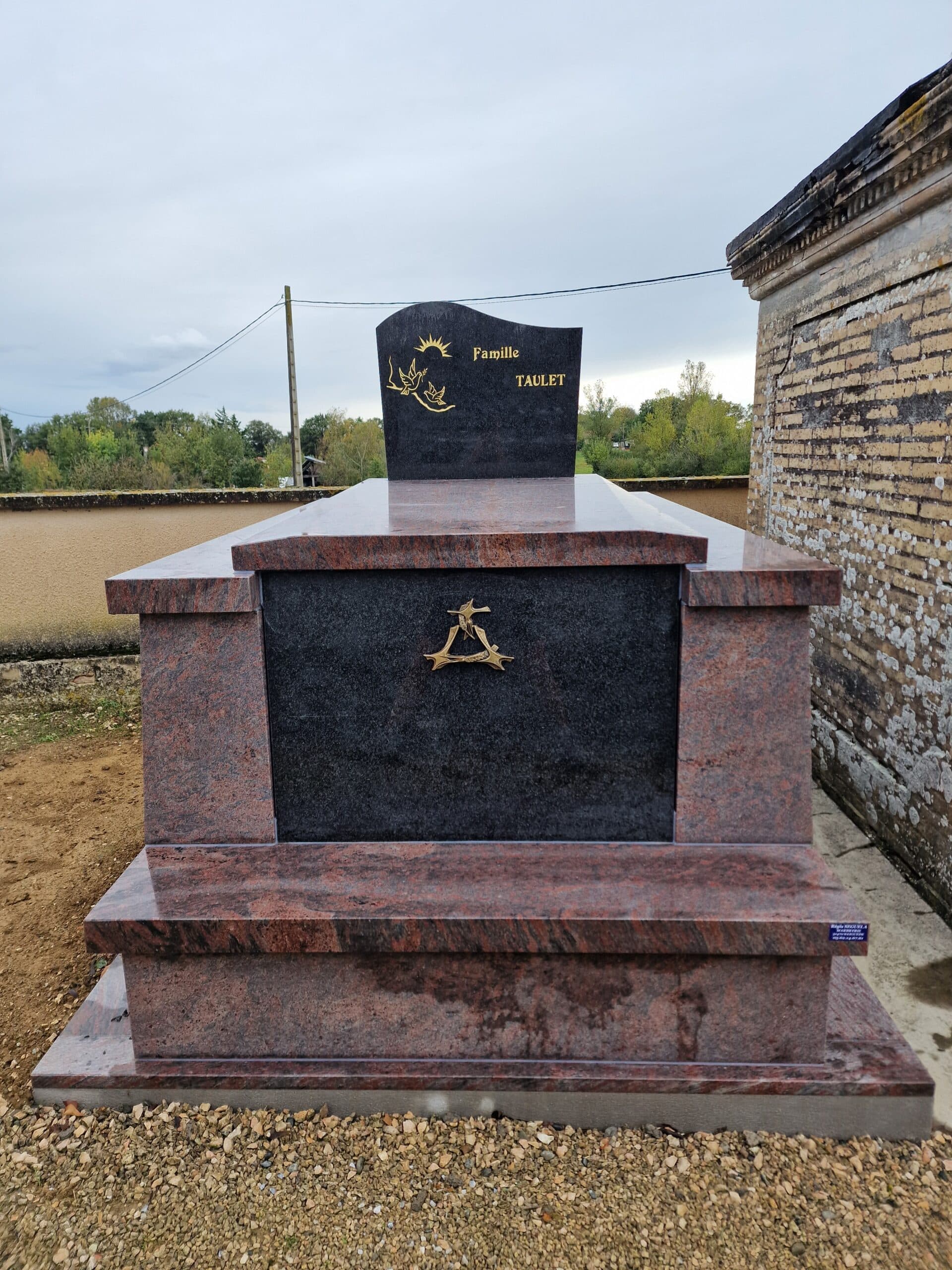 Tombe familiale en granit poli rouge et noir inscrite Famille Taulet avec décorations dorées dans un cimetière.