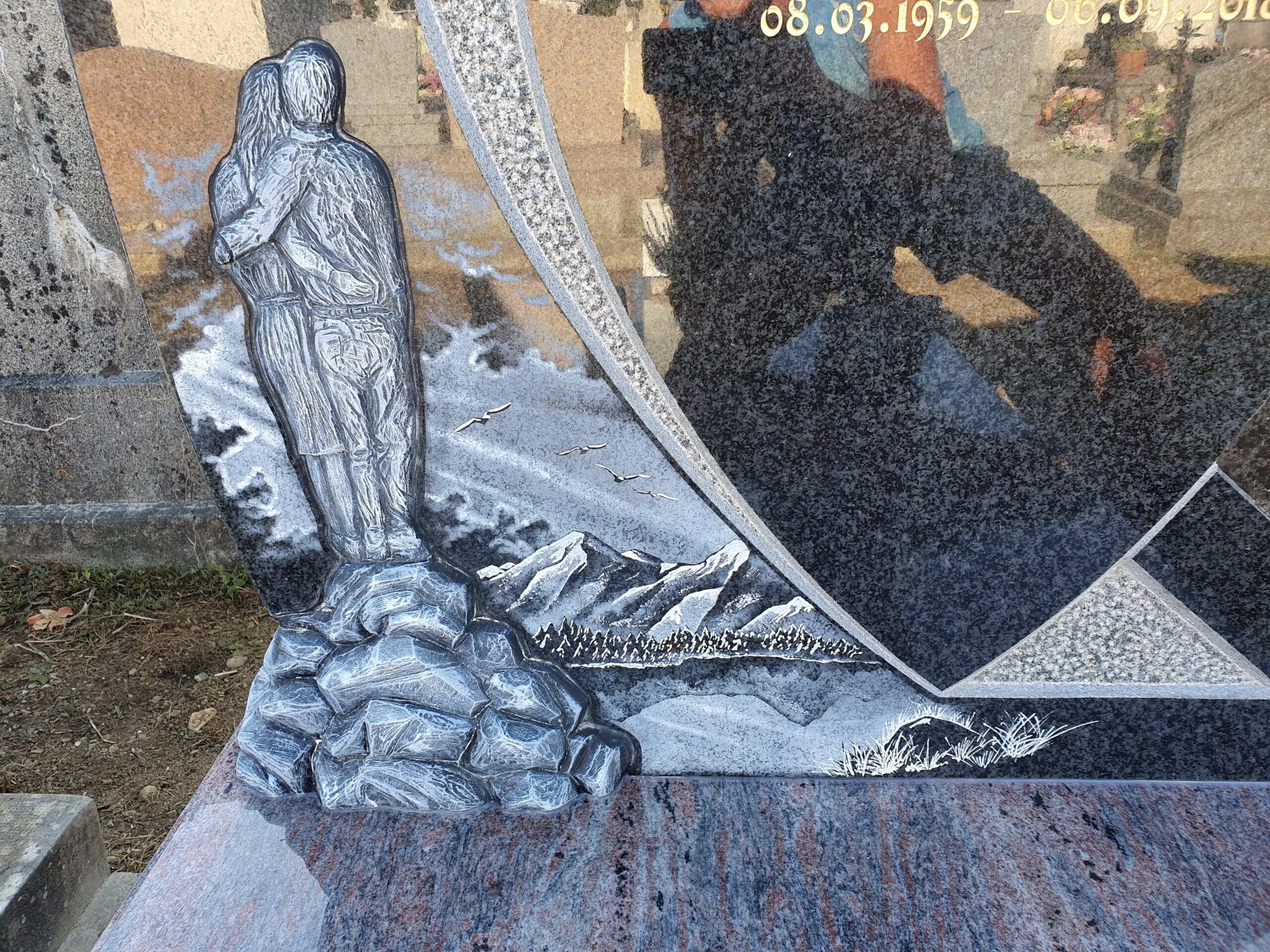 Gravure d'un couple enlacé sur monument funéraire en granit, avec décor de montagnes, forêt et oiseaux.