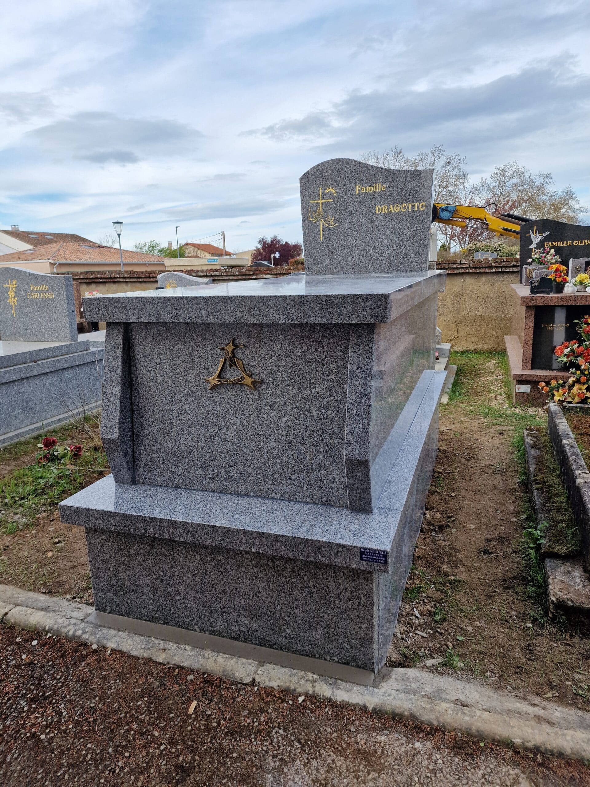 Monument funéraire en granit gris de la Famille Dragotto avec croix dorée et emblème en bronze dans un cimetière.