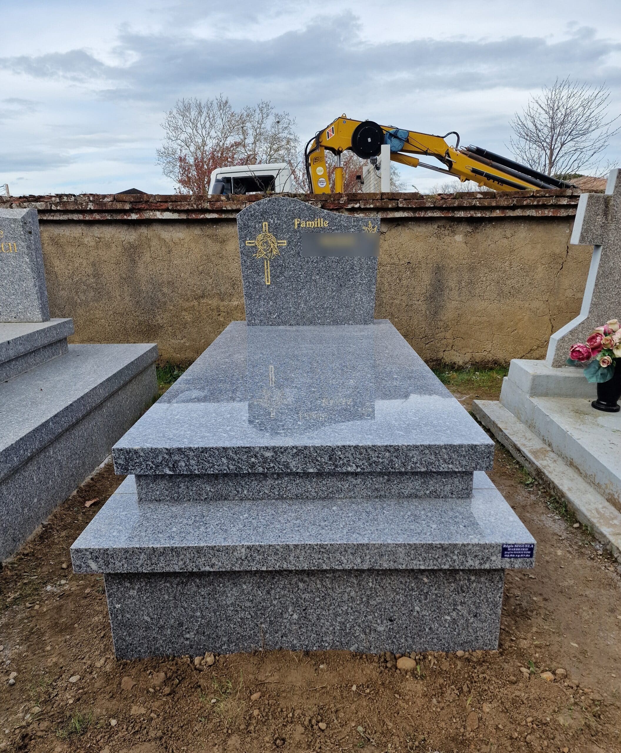 Monument funéraire en granit gris moucheté avec stèle gravée Famille et croix dorée dans un cimetière.