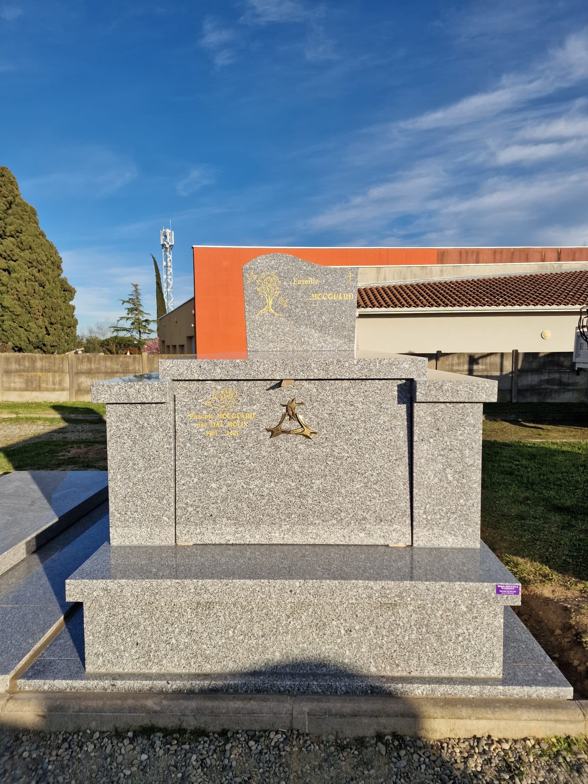 Monument funéraire en granit gris de la Famille Mocquard avec stèle gravée et décors dorés dans un cimetière ensoleillé.