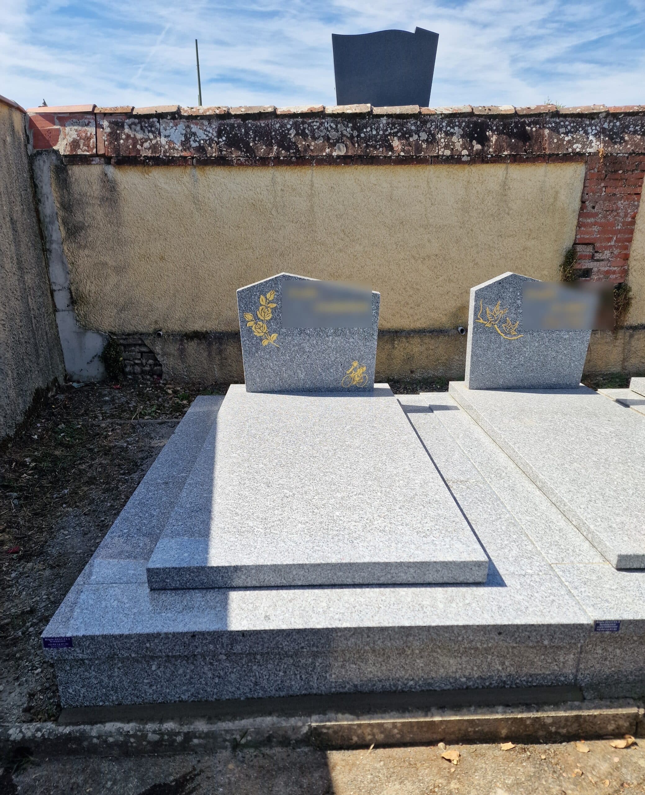 Monument funéraire en granit gris avec gravures dorées de fleurs et d'un cycliste sous un ciel bleu.
