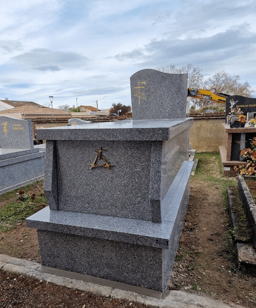 Tombe en granit gris poli avec gravures dorées et croix chrétienne dans un cimetière.