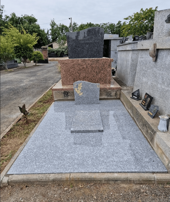 Monument funéraire en granit gris et rouge avec gravure florale dorée sur pierre tombale moderne.