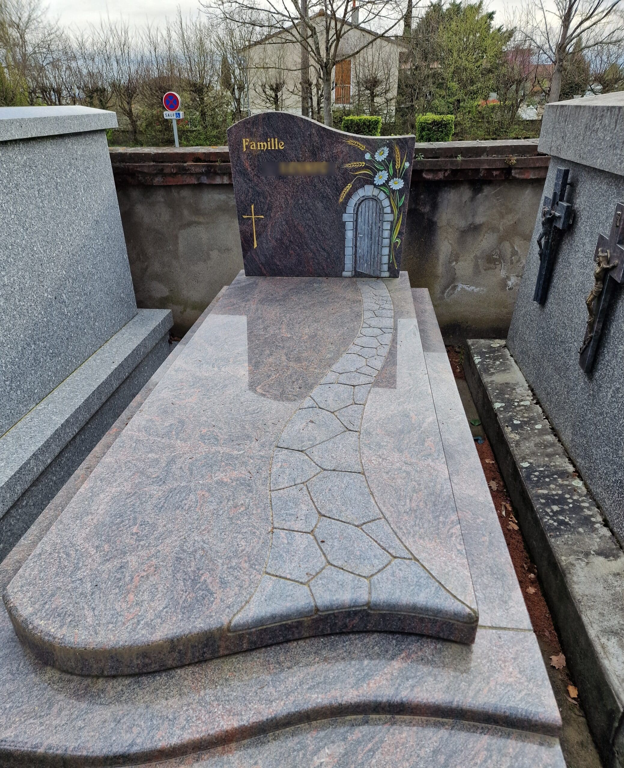 Monument funéraire en granit avec chemin sculpté, croix d'or et décor de porte fleurie. Inscription : Famille.