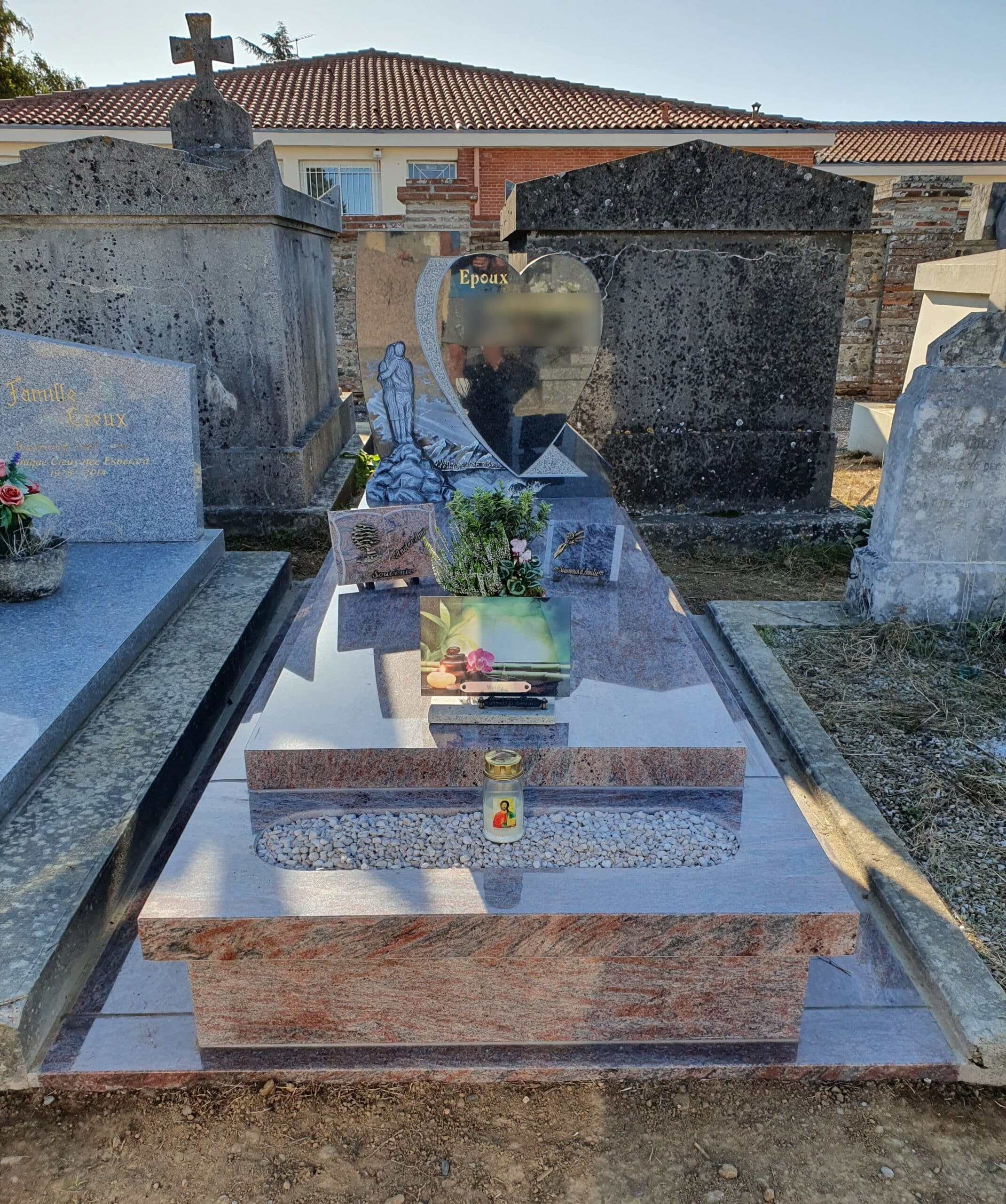 Monument funéraire en granit rose avec stèle en forme de cœur, inscription 'Epoux' et bougie dans un cimetière.