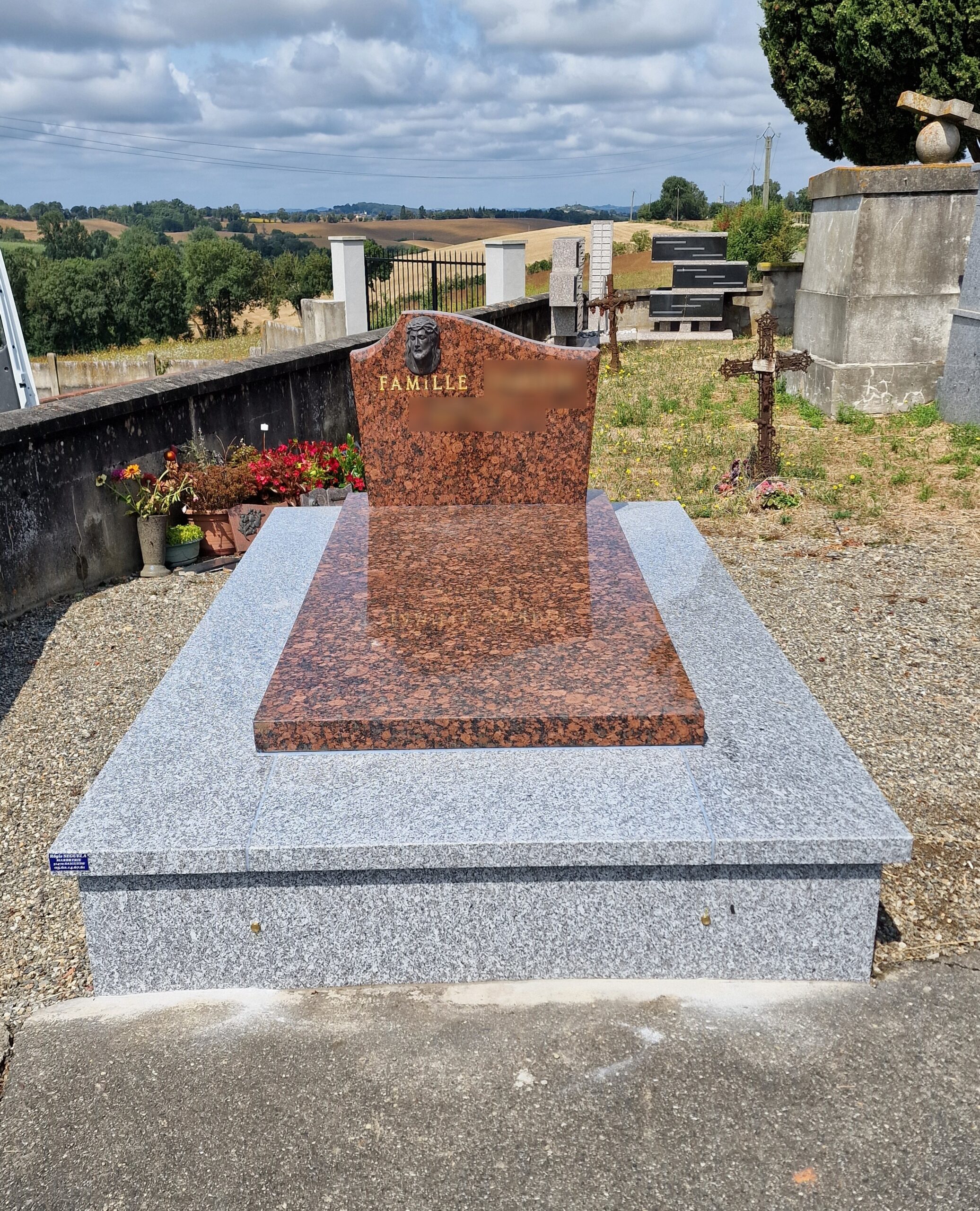 Monument funéraire en granit bicolore rouge et gris avec inscription Famille et visage du Christ dans un cimetière.