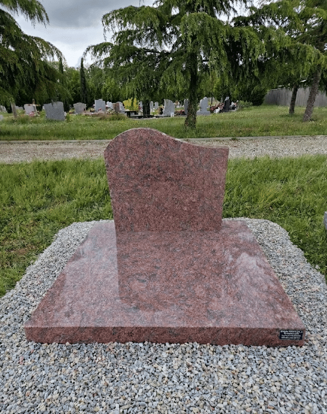 Monument funéraire en granit rouge flammé au design moderne dans un cimetière verdoyant et paisible.