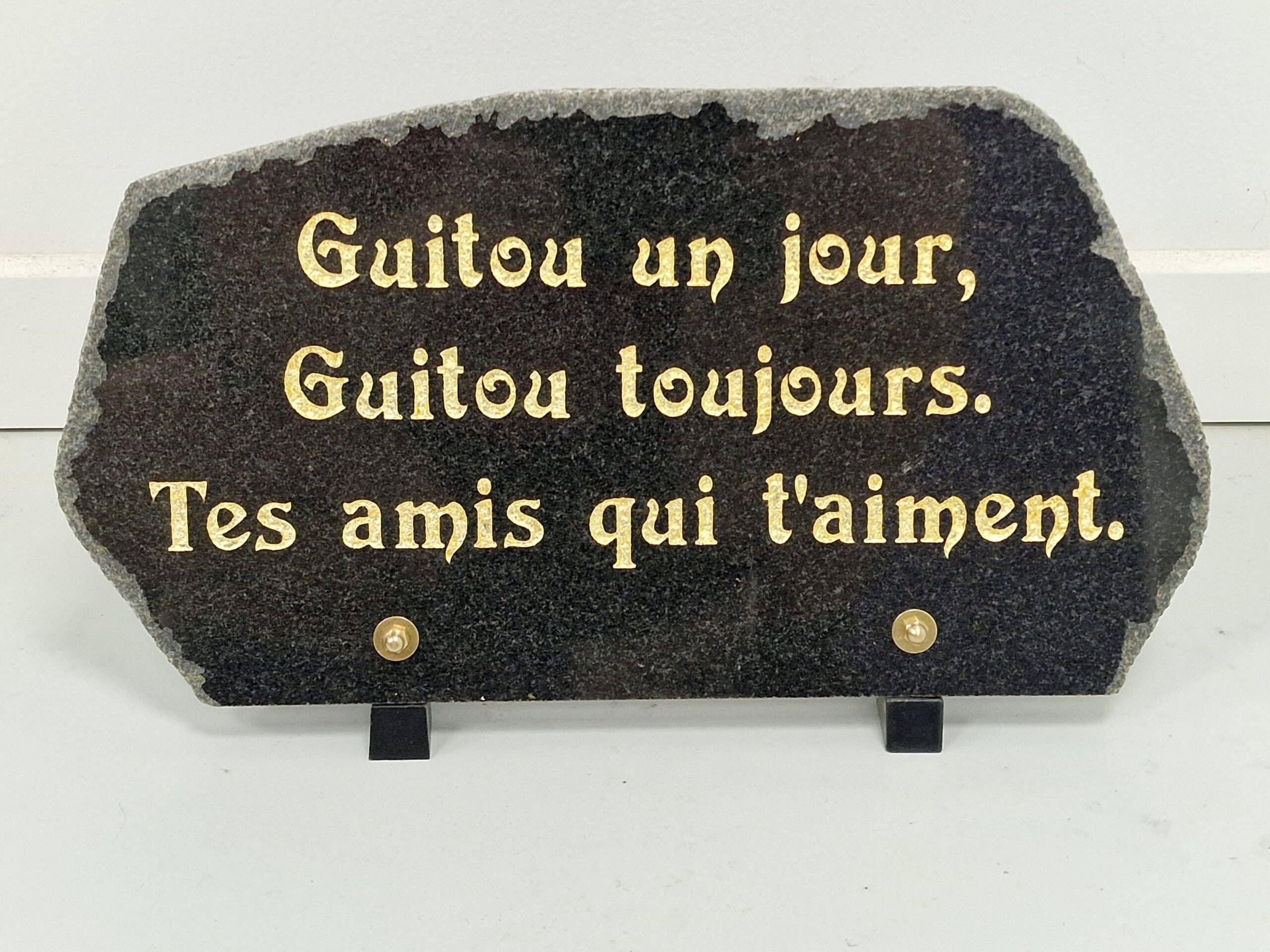Plaque commémorative en granit noir avec texte doré : Guitou un jour, Guitou toujours. Tes amis qui t'aiment.