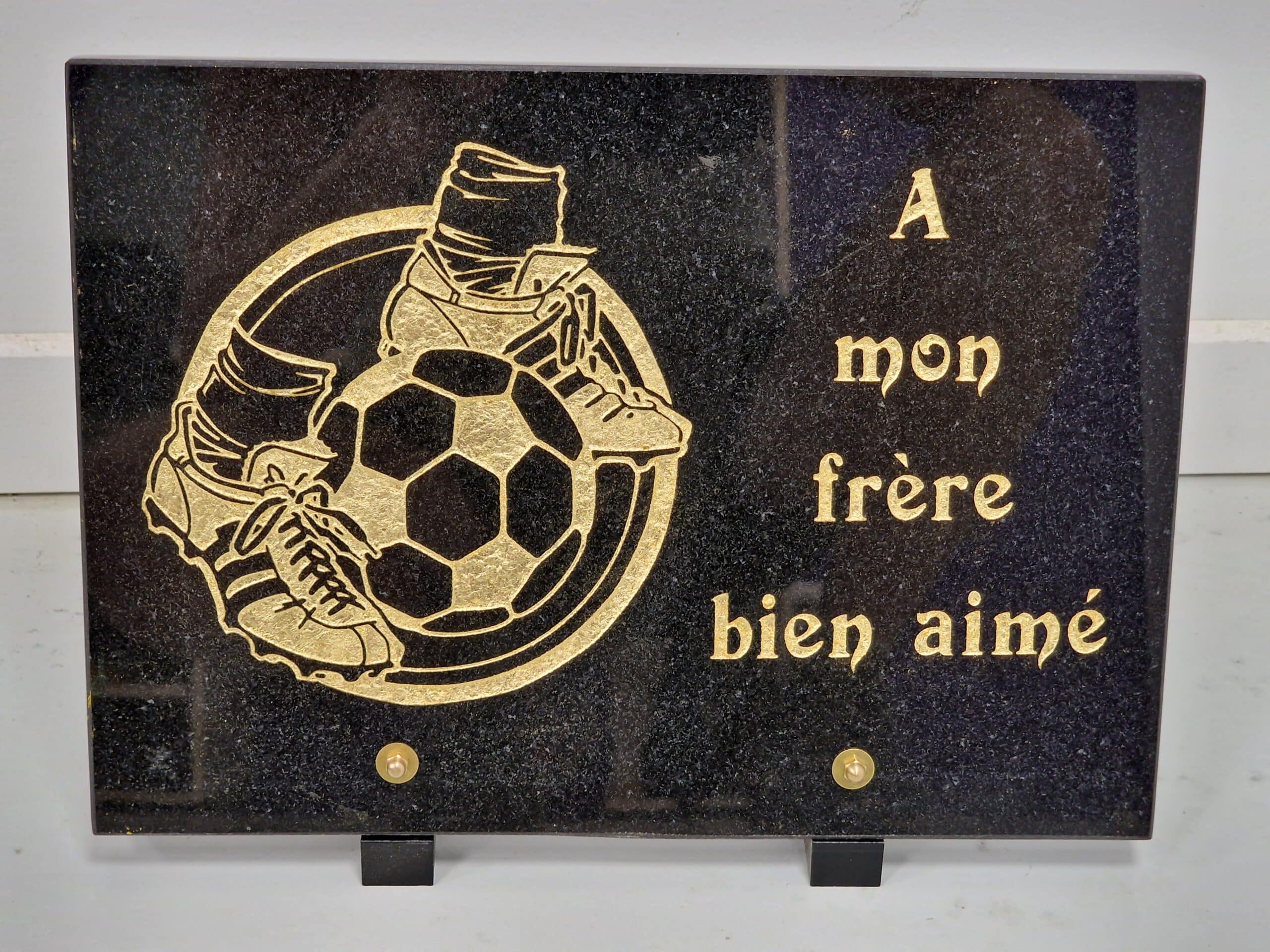 Plaque funéraire en granit noir avec gravure dorée de football et texte 'À mon frère bien aimé'.