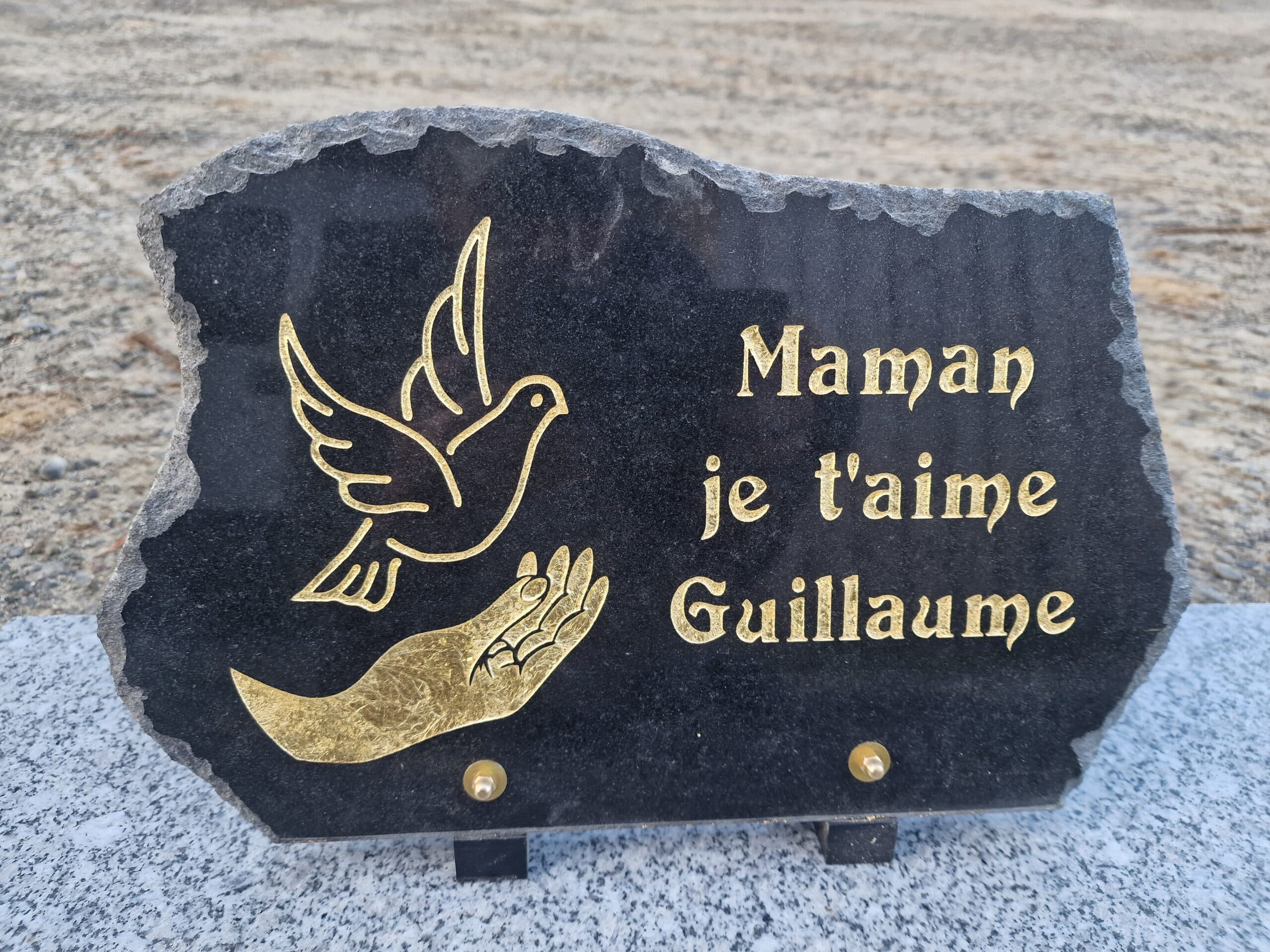 Plaque funéraire en pierre noire, gravure dorée d'une colombe et texte "Maman je t'aime Guillaume".