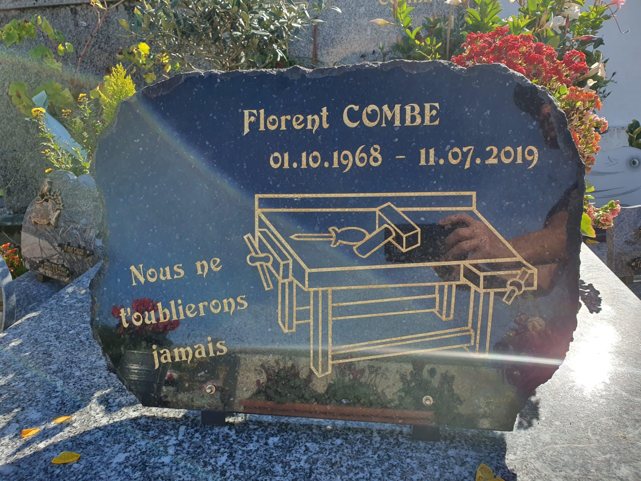 Plaque funéraire de Florent Combe avec gravure d'établi et texte 'Nous ne t'oublierons jamais' en lettres dorées.