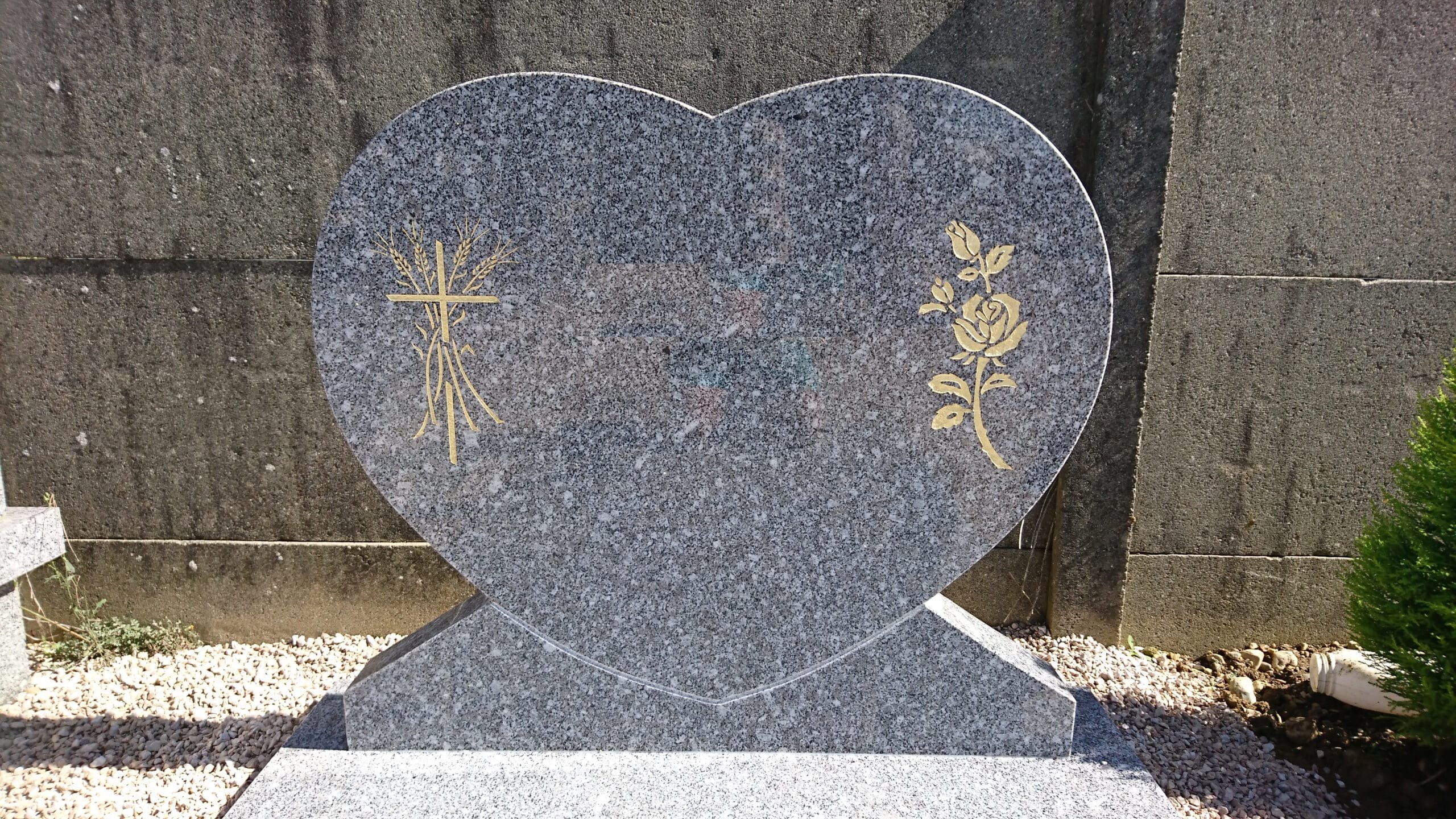 Pierre tombale en granit gris en forme de cœur avec gravures dorées d'une croix et d'une rose.