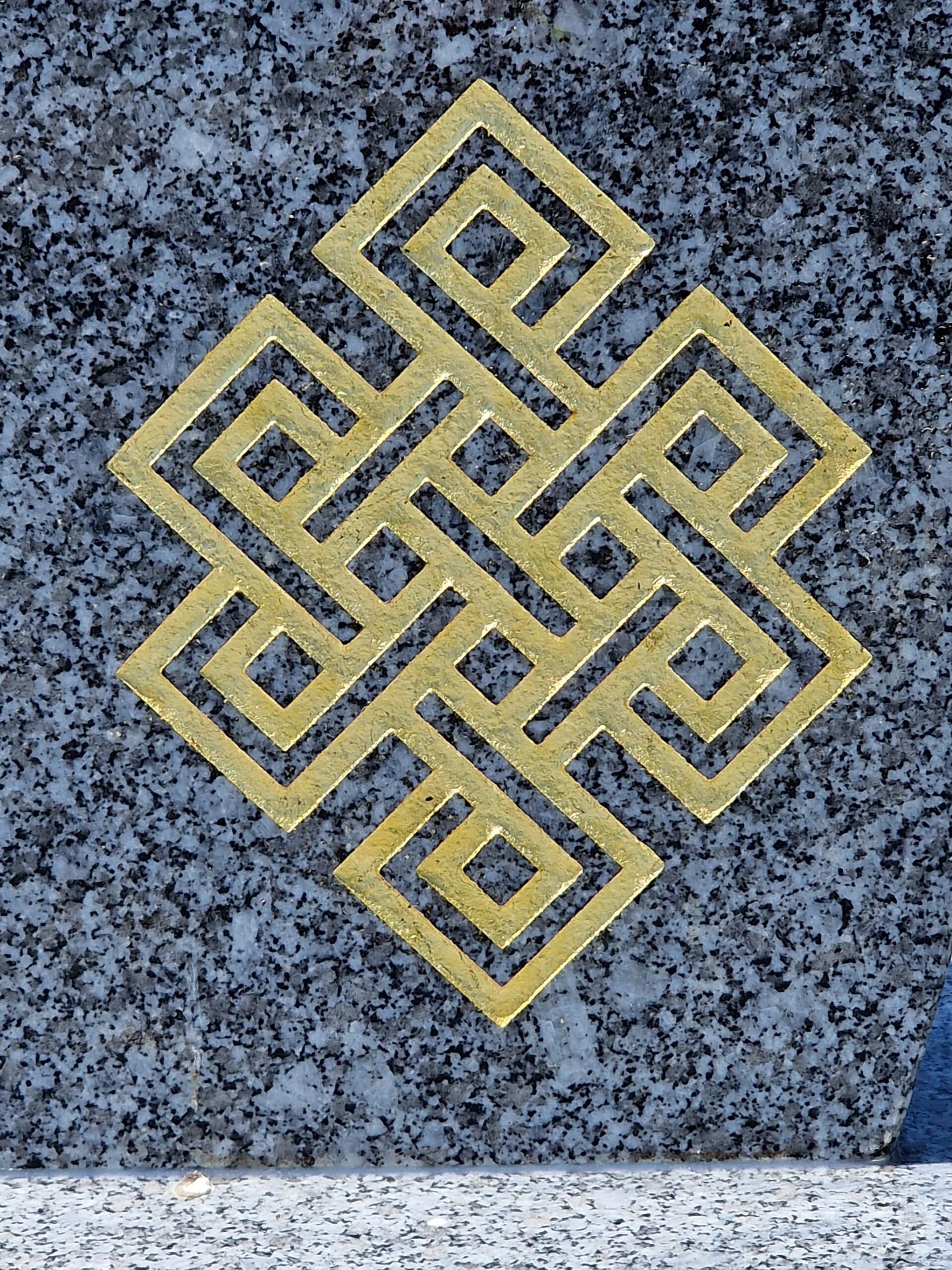 Symbole doré du nœud sans fin bouddhiste gravé sur une pierre de granite grise tachetée, représentant l'harmonie.