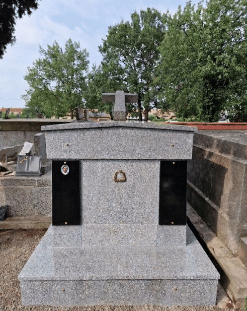 Monument funéraire en granit gris avec croix, plaques noires et médaillon photo dans un cimetière.