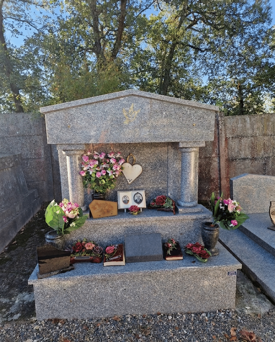 Monument funéraire en granit gris avec colonnes, fleurs roses, colombe dorée et médaillons photos commémoratifs.