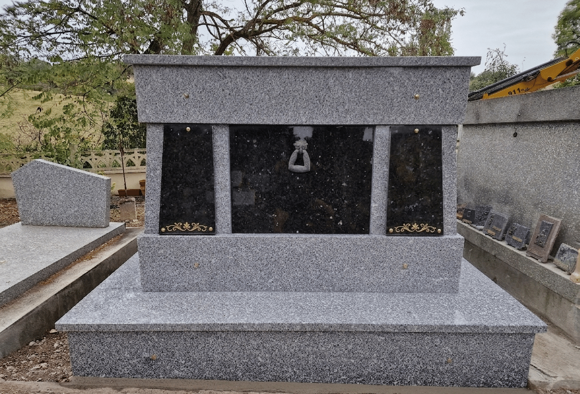 Monument funéraire moderne en granit gris et noir avec ornements dorés et anneau central dans un cimetière.