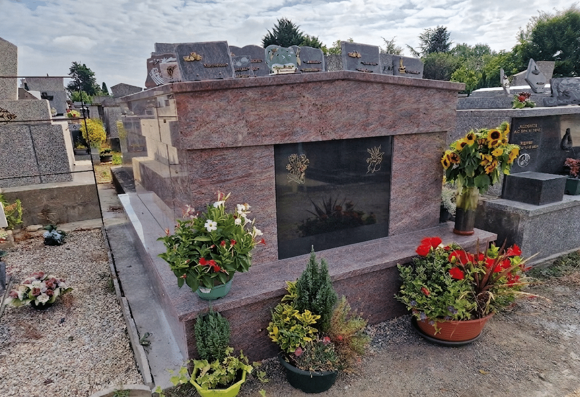 Monument funéraire en granit rose orné de fleurs colorées et plaques commémoratives dans un cimetière.