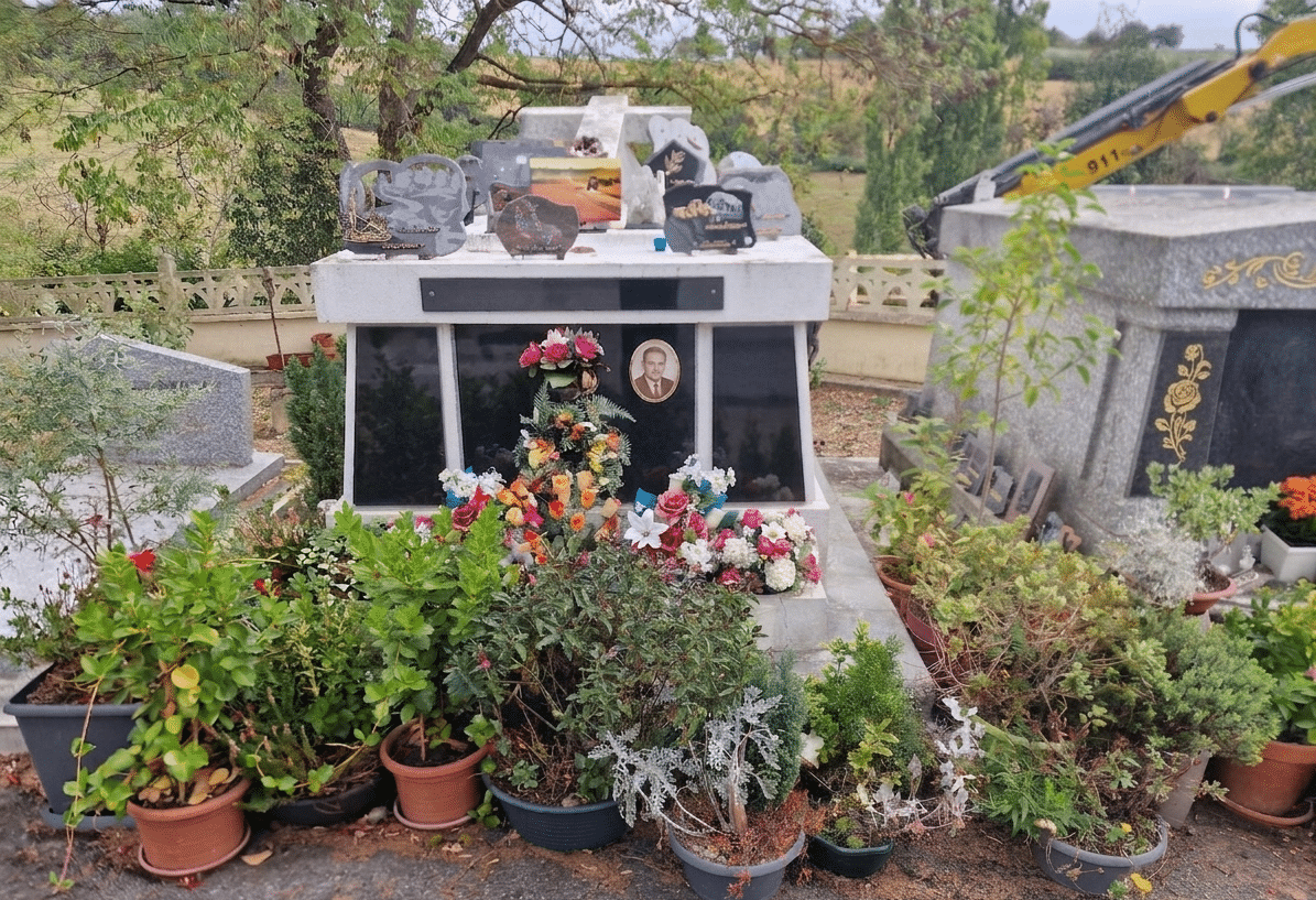 Tombe fleurie avec portrait et plaques commémoratives, nombreux pots de fleurs au pied d'un monument funéraire.