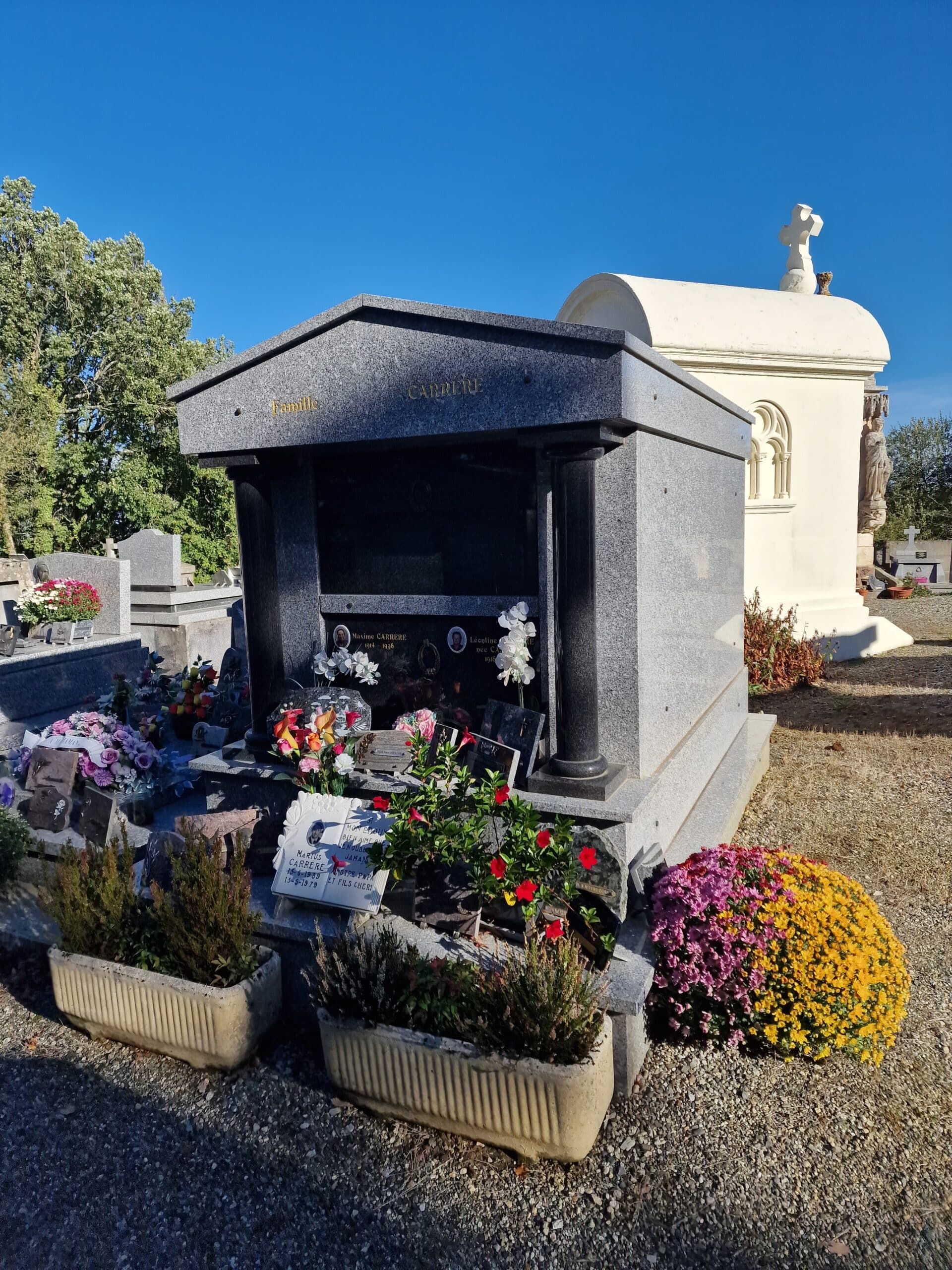 Tombeau en granit Famille Carrere orné de fleurs colorées sous un ciel bleu dégagé au cimetière.