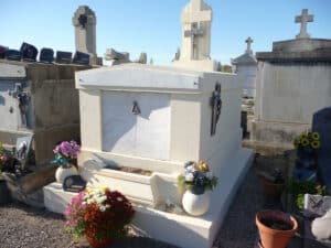 Tombe mausolée blanche avec crucifix et marbre, décorée de chrysanthèmes et fleurs artificielles dans un cimetière français.