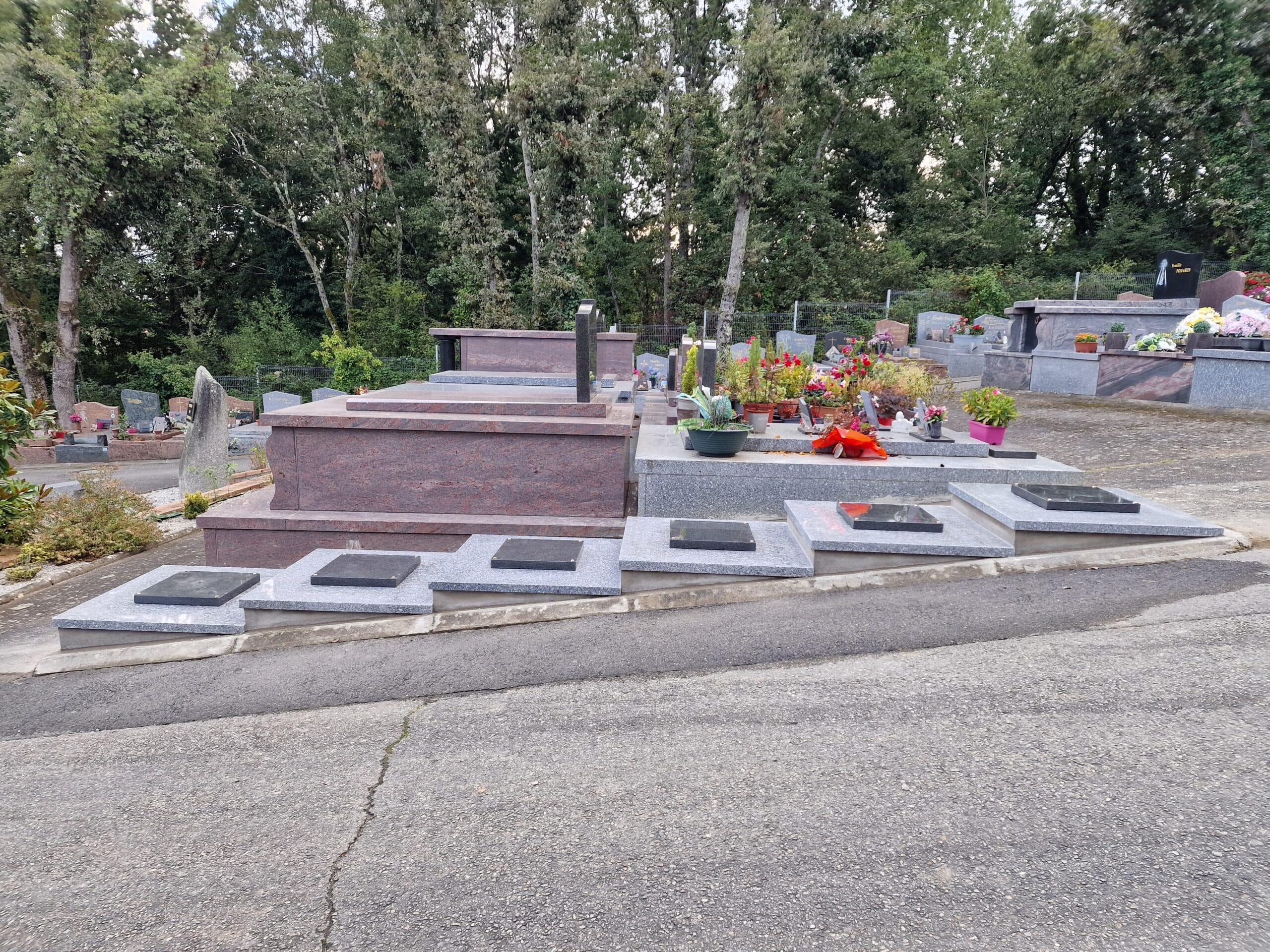 Monuments funéraires en granit et caveau familial fleuri dans un cimetière arboré, mention Famille Pomarès visible.