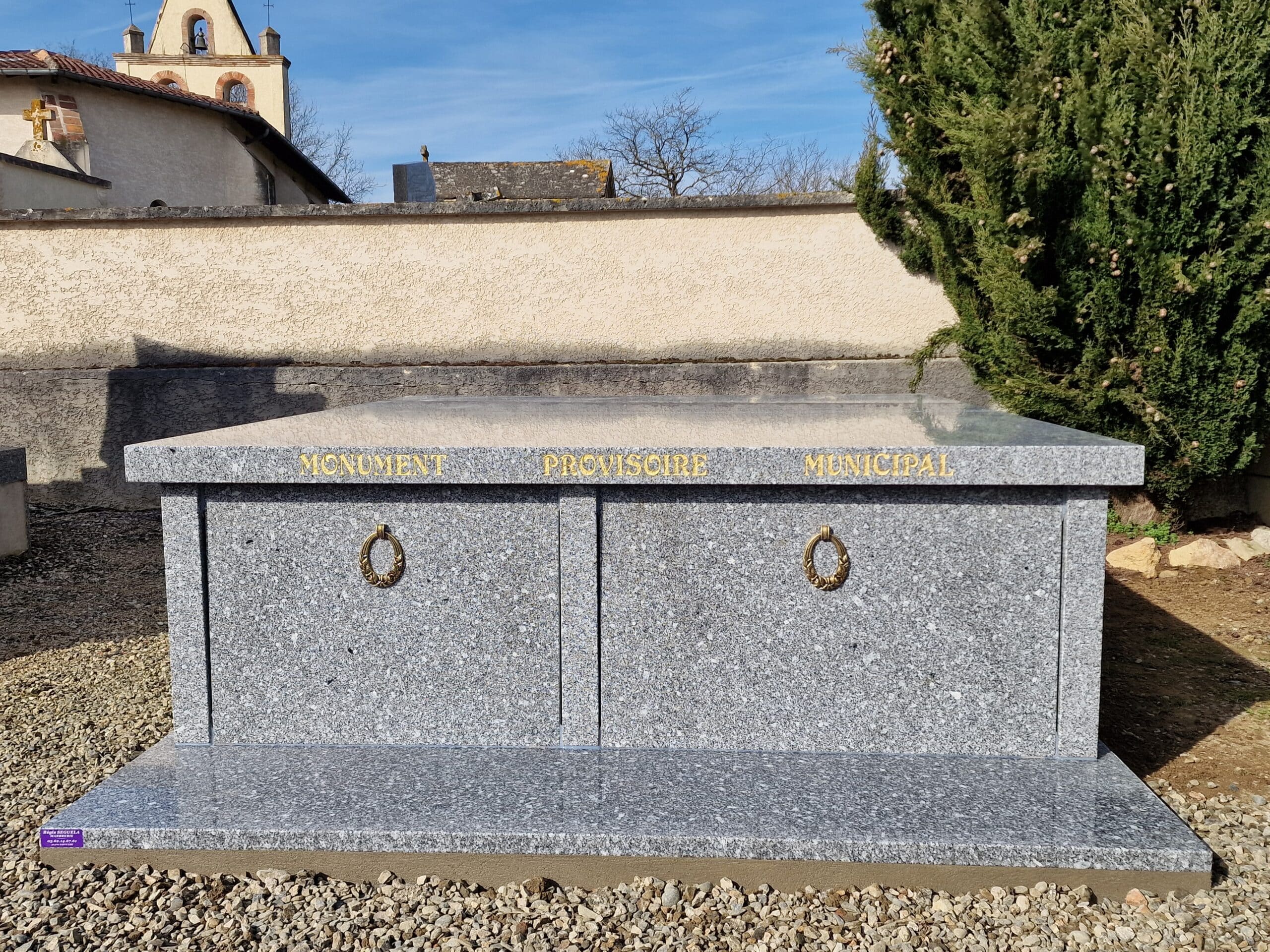 Monument provisoire municipal en granit gris avec inscriptions dorées dans un cimetière ensoleillé.